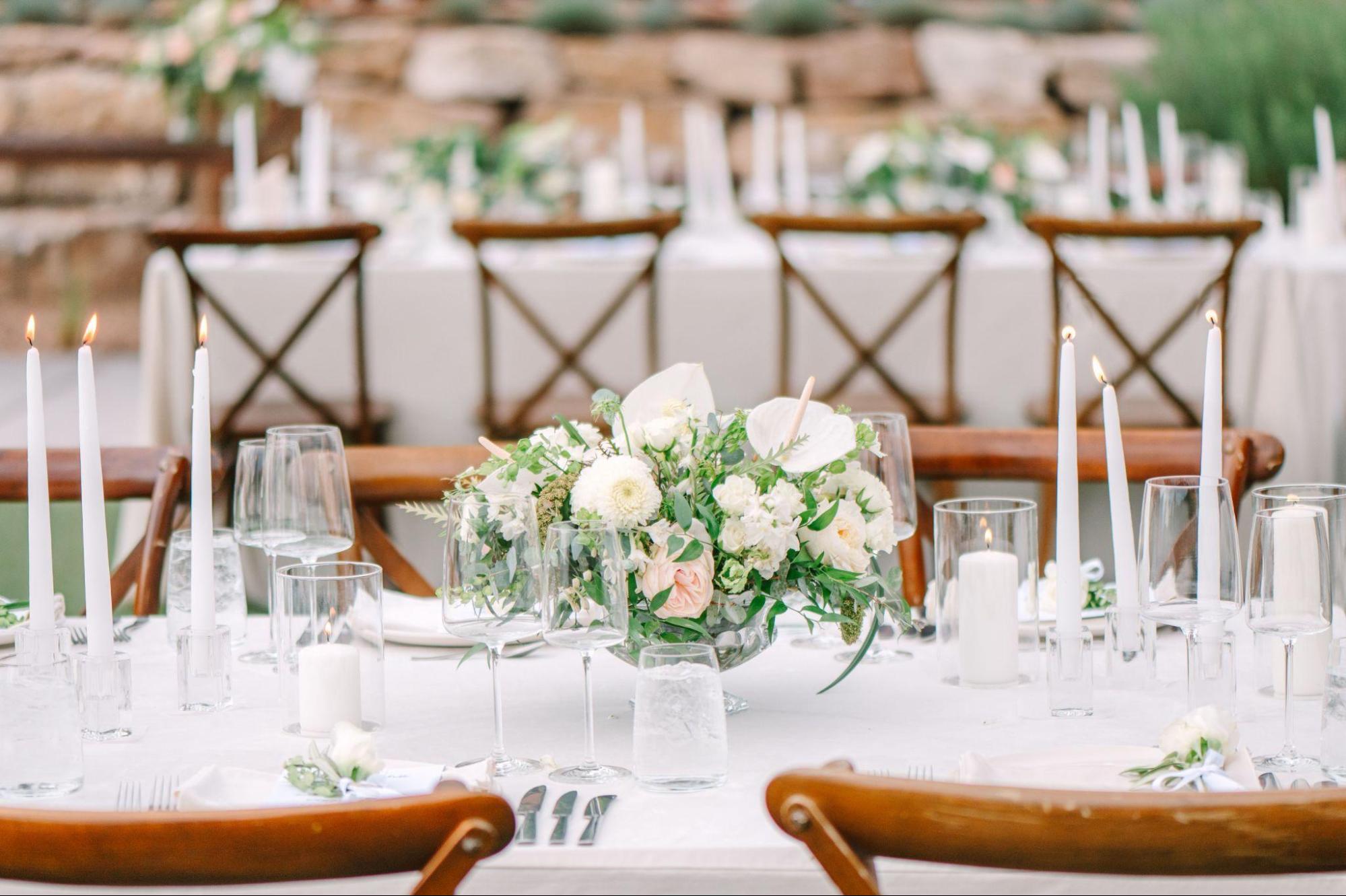 This photo features an elegant wedding table setting with a floral centerpiece, taper candles, glassware, and wooden chairs, showcasing a beautiful and romantic ambiance. Set up by a New Mexico wedding planner.