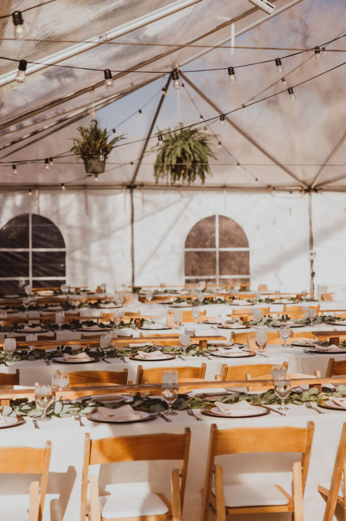 Elegant wedding reception setup in a tent with wooden chairs and green decor, showcasing the attention to detail in full-service wedding planning.