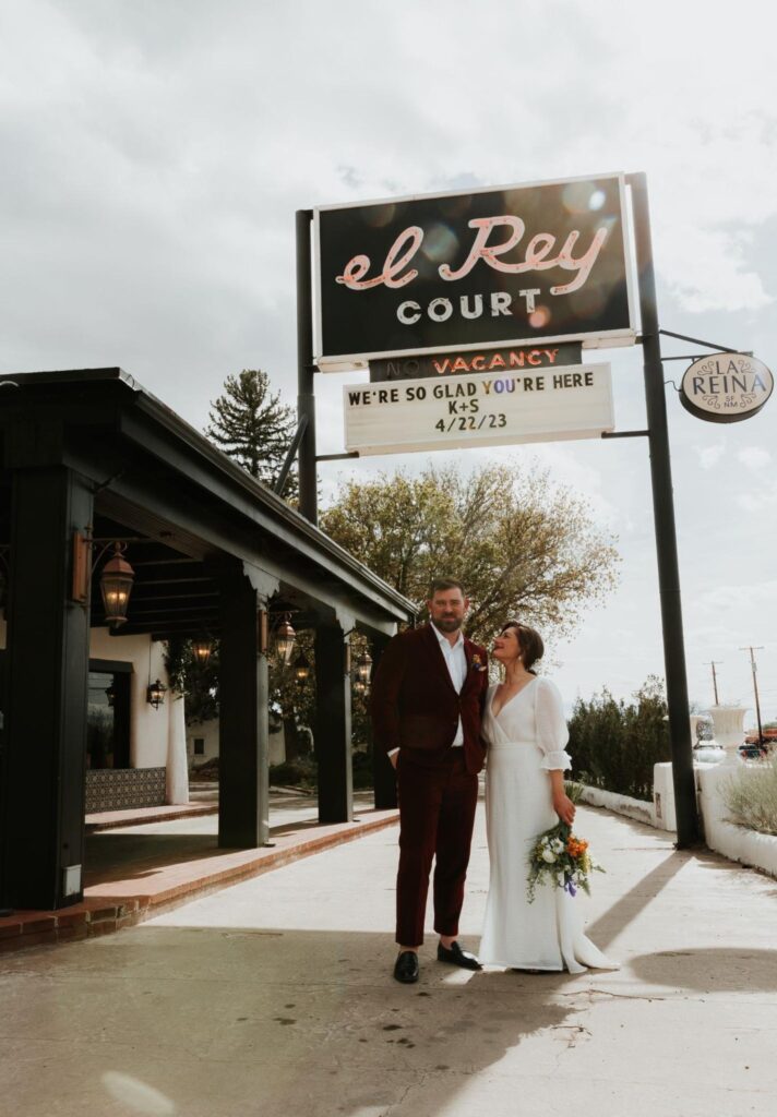 The newlyweds pose beneath the vintage "El Rey Court" sign, which displays a custom welcome message for their wedding day. 