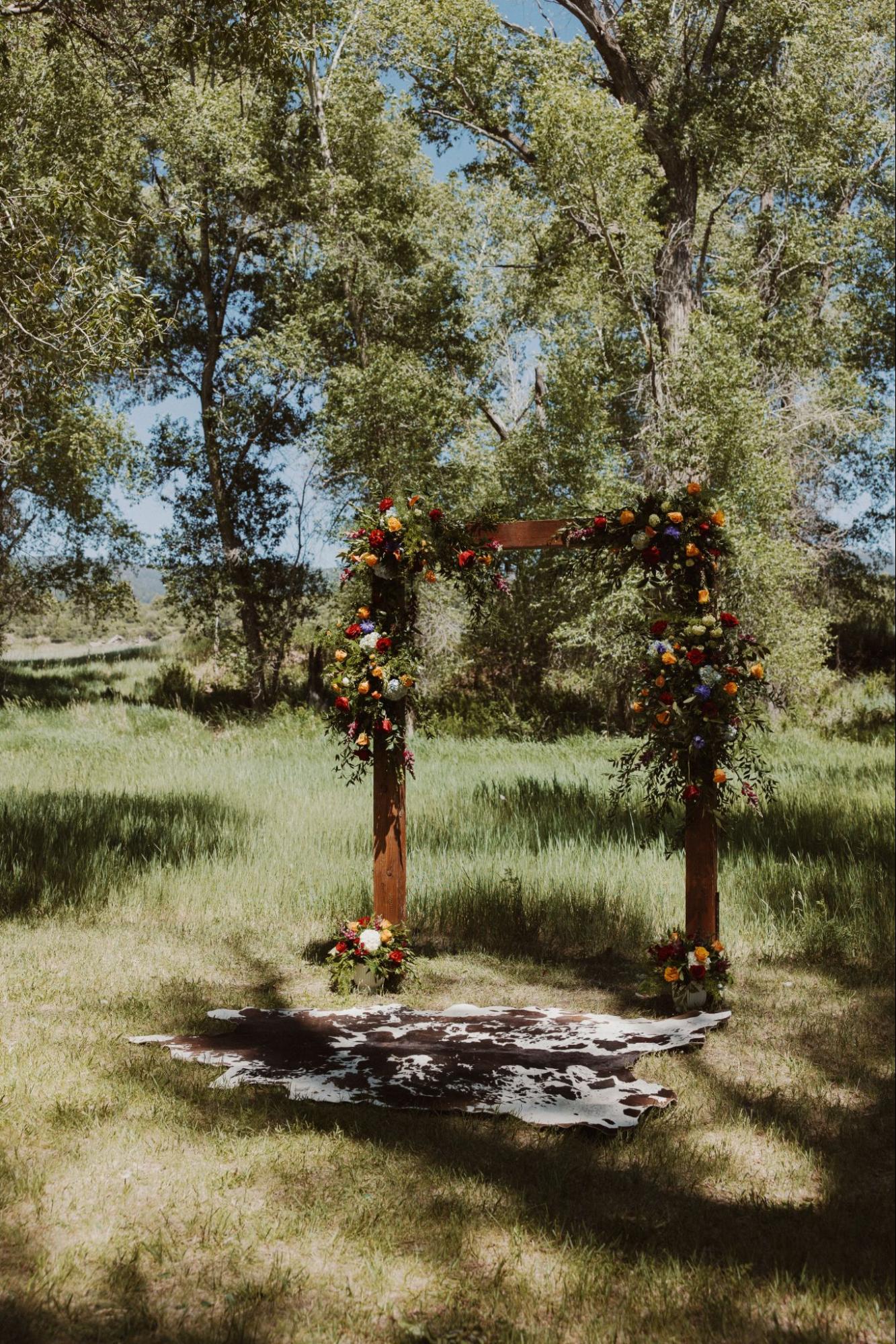 a rustic outdoor wedding arch adorned with vibrant floral arrangements, set in a natural grassy landscape | wedding planning guide