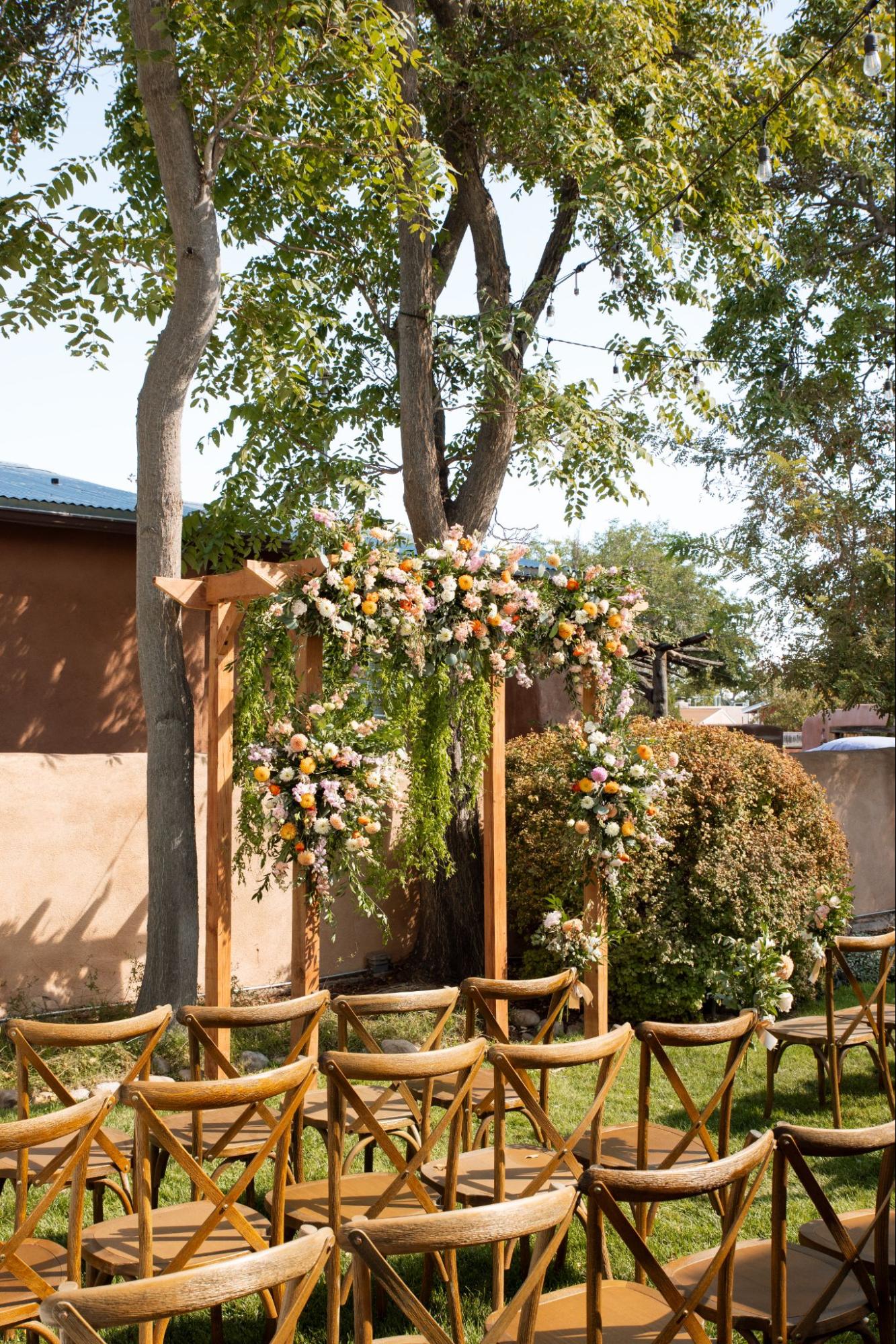 Outdoor ceremony with wooden arbor, cascading florals, and rustic chairs embodying nature-inspired 2025 wedding trends.