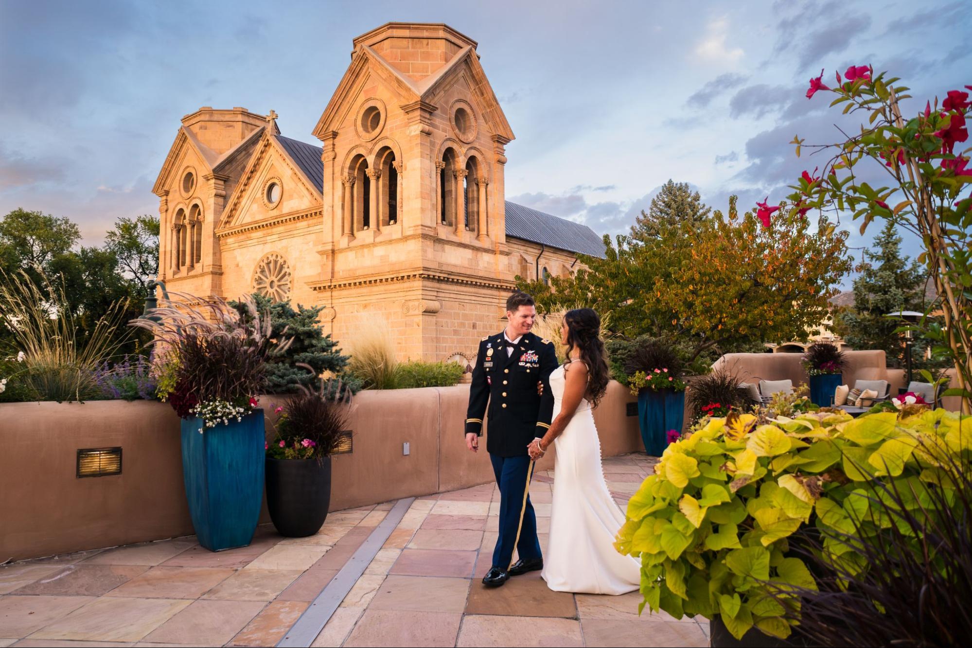 A stunning couple poses outside a historic Santa Fe church during their wedding weekend in Santa Fe, surrounded by vibrant flowers.