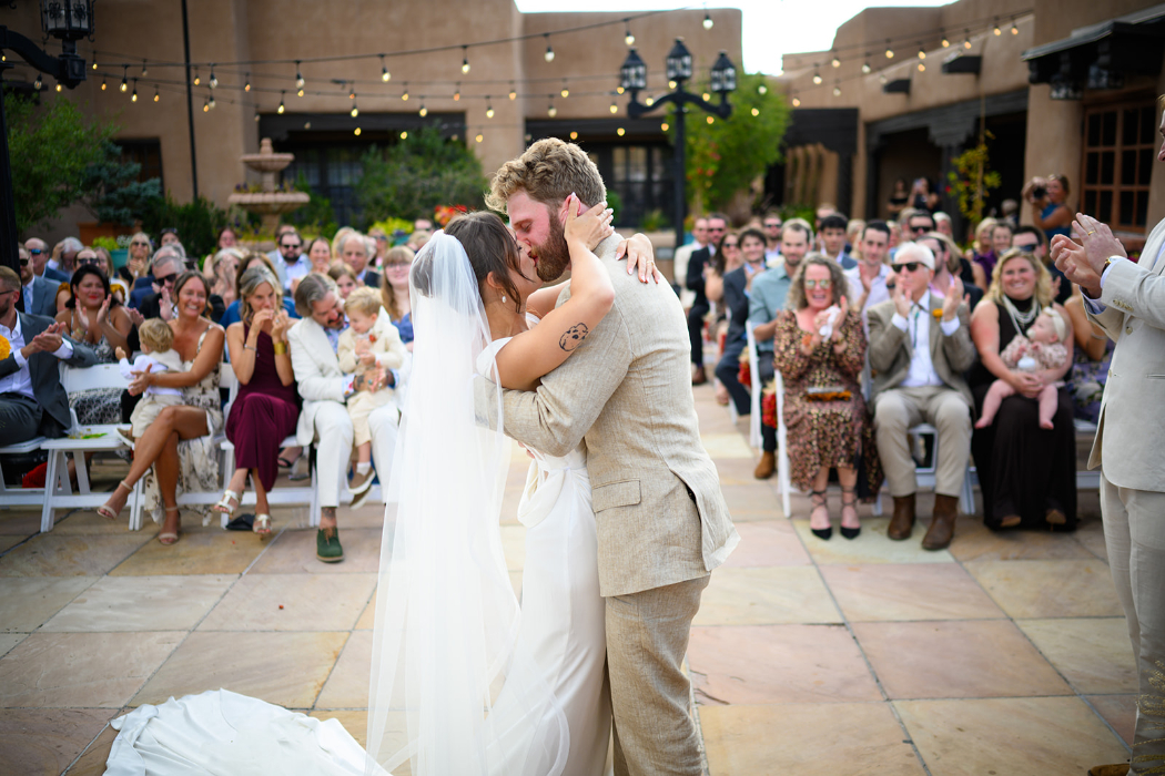 A bride and groom share their first kiss as a married couple in an outdoor courtyard ceremony.