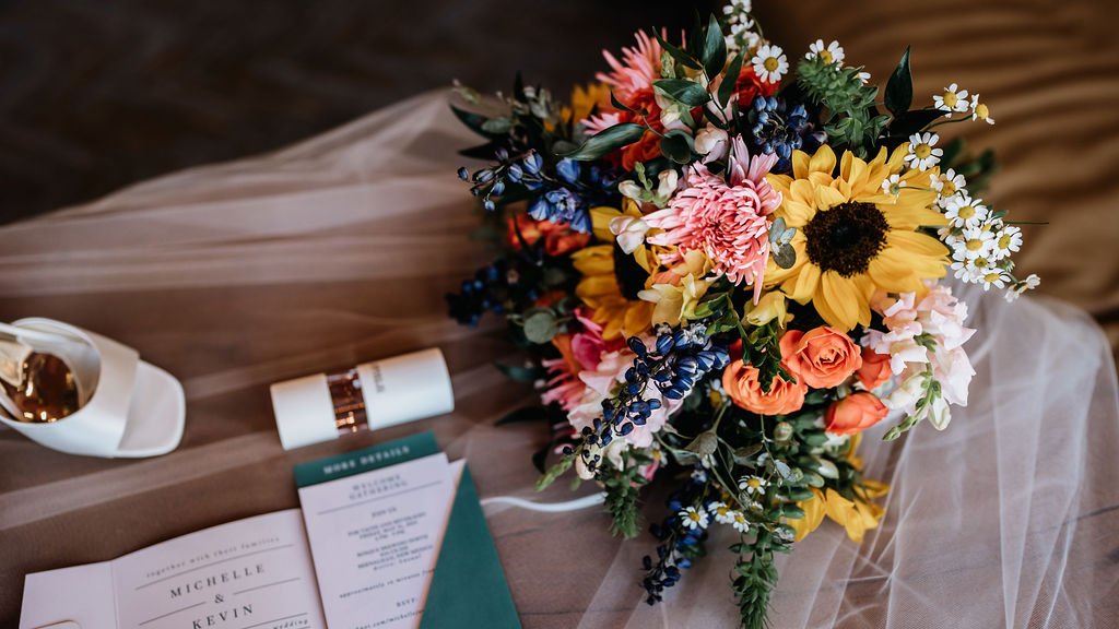 A vibrant wedding bouquet with sunflowers, roses, and wildflowers rests beside flatlay details.
