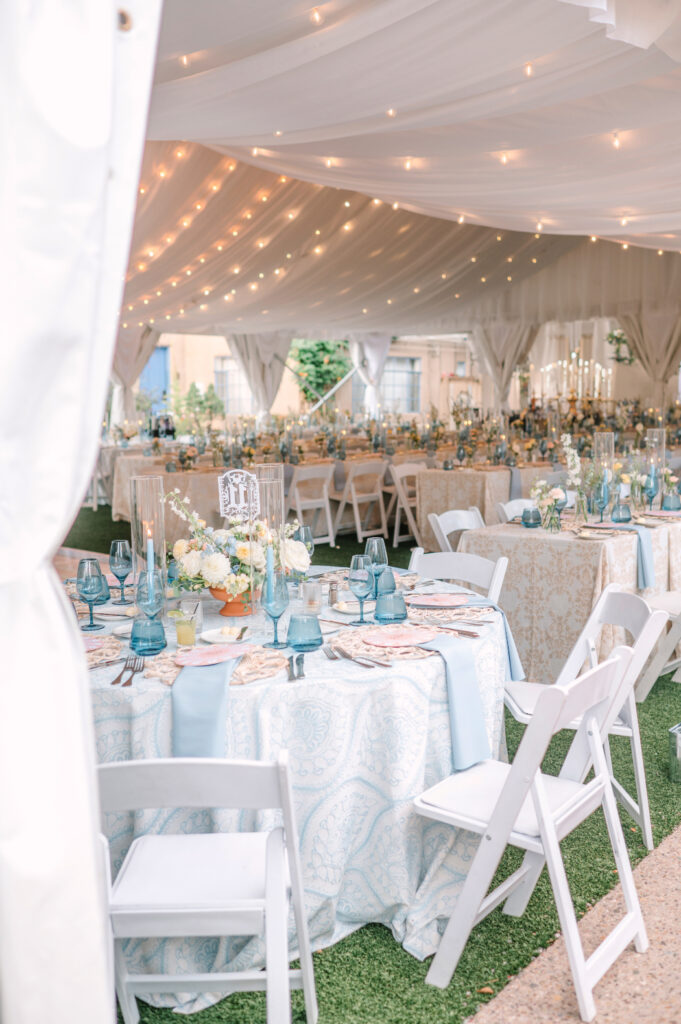 Reception tables inside the tent at La Posada in Santa Fe, styled with soft linens, blue glassware, and candlelight under draped string lights.