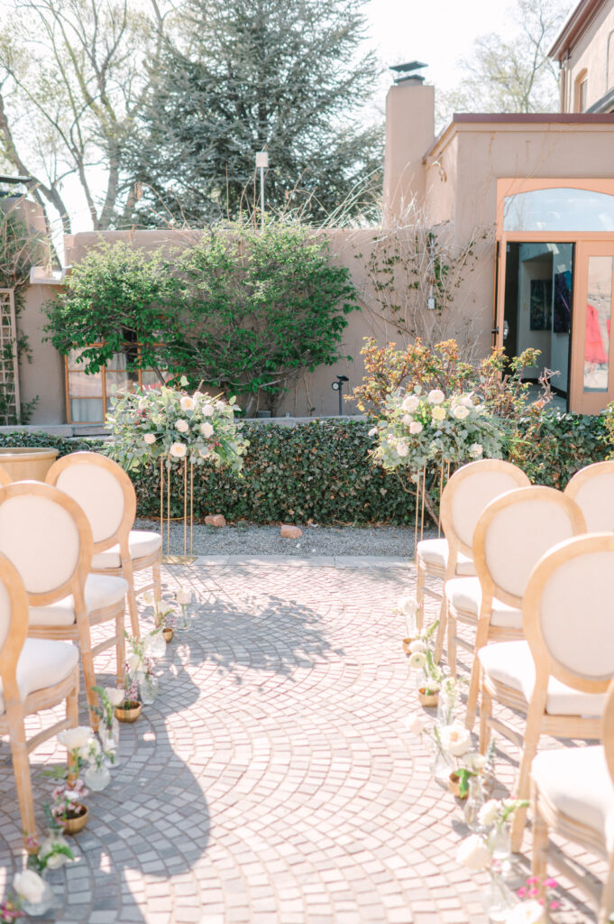 A ceremony setup at La Posada in Santa Fe, with elegant chairs and low floral arrangements lining the aisle.