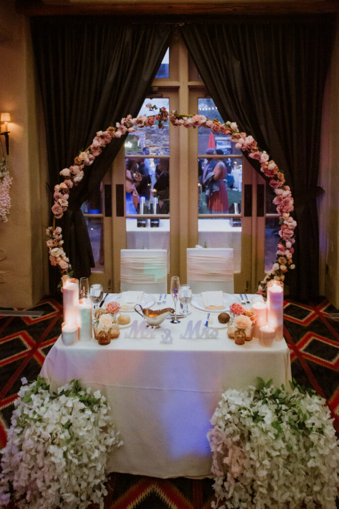 Sweetheart table with circular floral arch and soft candlelight. Romantic indoor setup featuring custom floral installation by florists in Santa Fe.