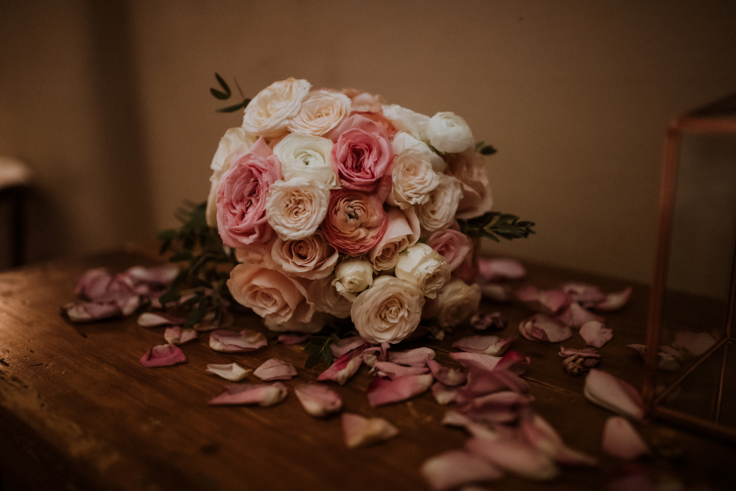 Classic round bouquet with white, blush, and pink roses surrounded by scattered petals. A timeless arrangement by florists in Santa Fe for an elegant bridal look.