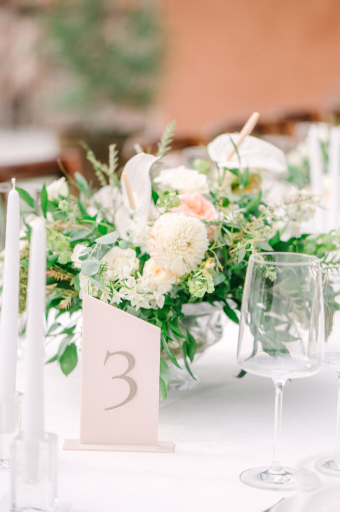 Neutral-toned table centerpiece with white and blush flowers, taper candles, and glassware.