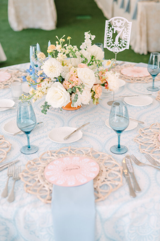 Vibrant round table setting with pastel flowers, blue glassware, and woven chargers. Showcasing a mix of color and texture for a spring wedding.