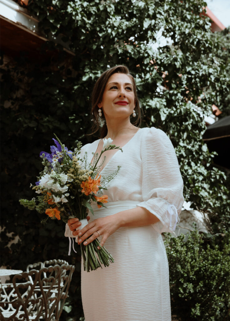 Bride dressed in white flowy wedding dress holding colorful bouquet.