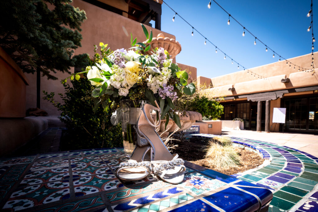 Elegant heels and bouquet on a tiled fountain in a sunny courtyard.