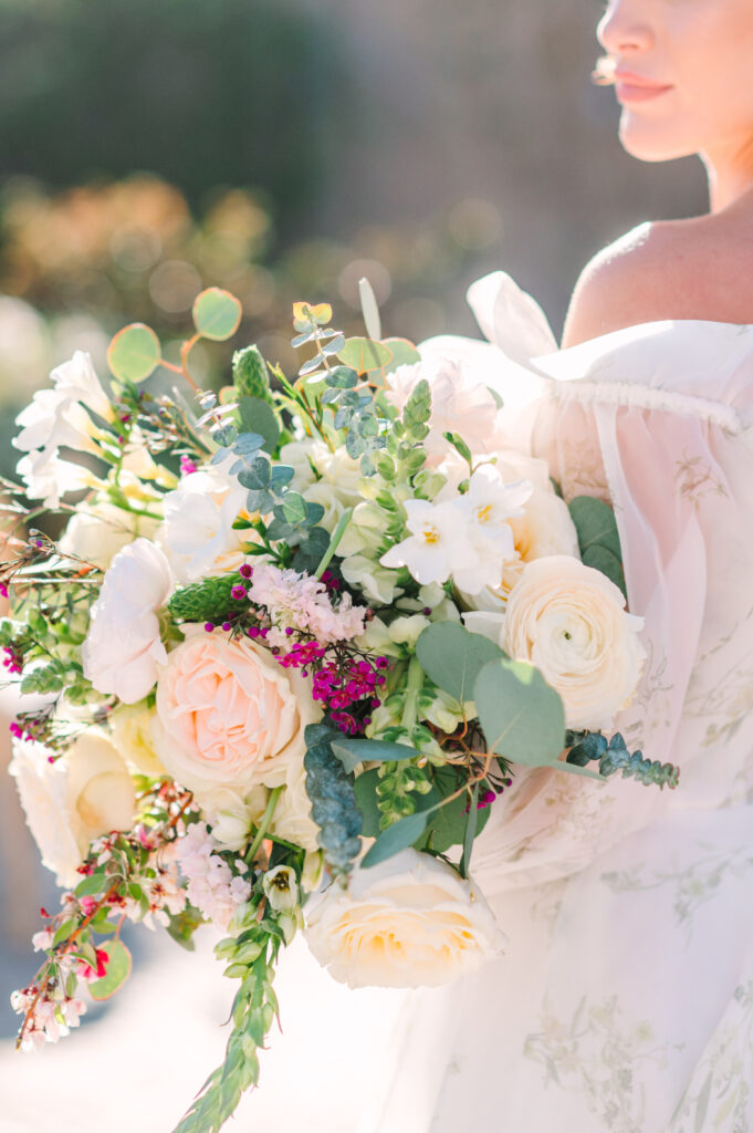 Bride holding a pastel floral bouquet in soft sunlight.