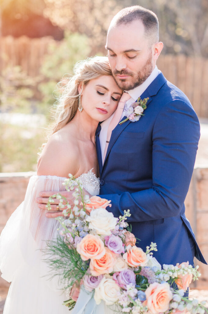 Bride and groom embracing, holding a colorful bouquet.