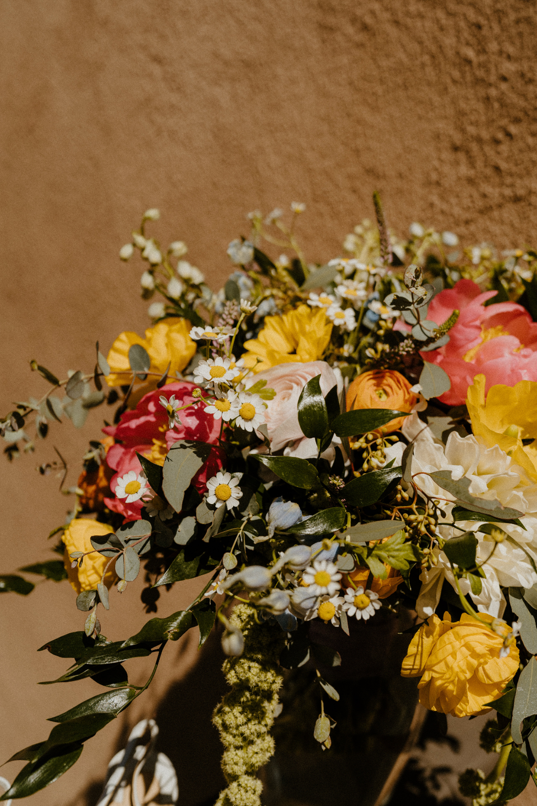 Bright yellow, soft blush, and coral blooms are mixed with white daisies and greenery for a cheerful, slightly wild bouquet.