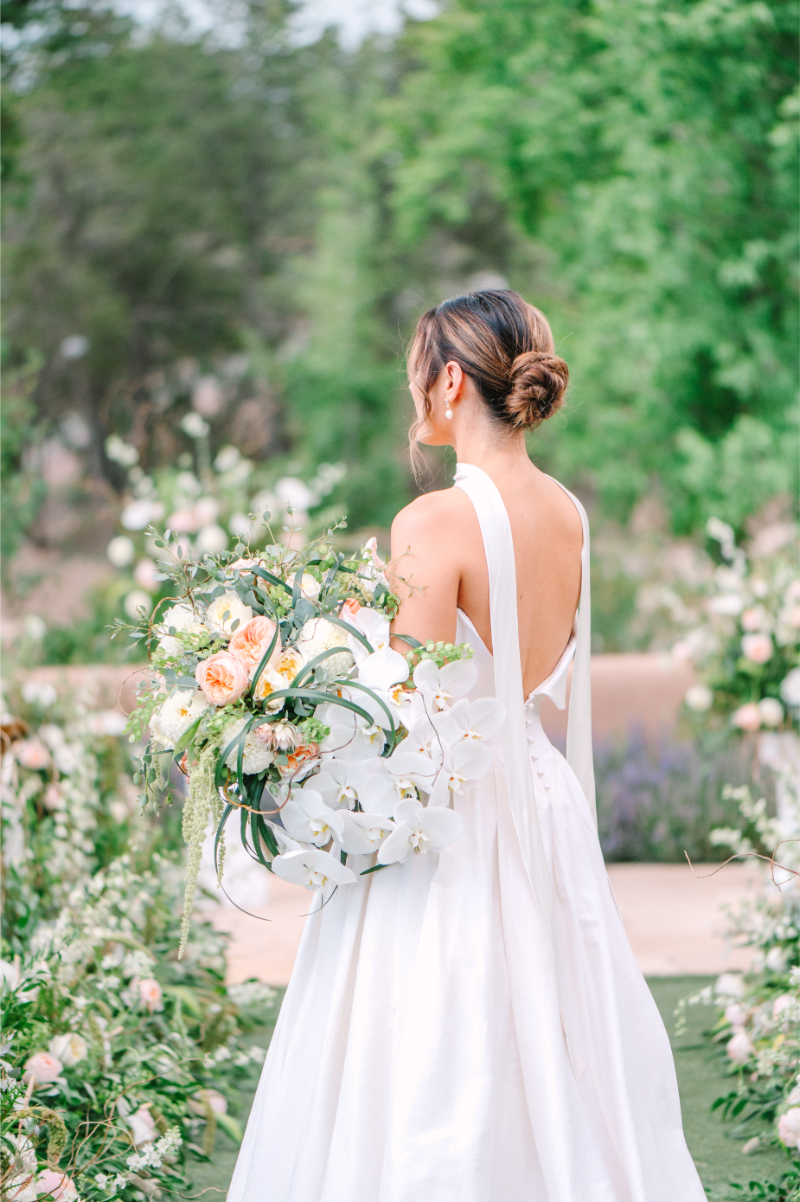 Bride holds luxury flower bouquet as she stands in center of wedding ceremony aisle.