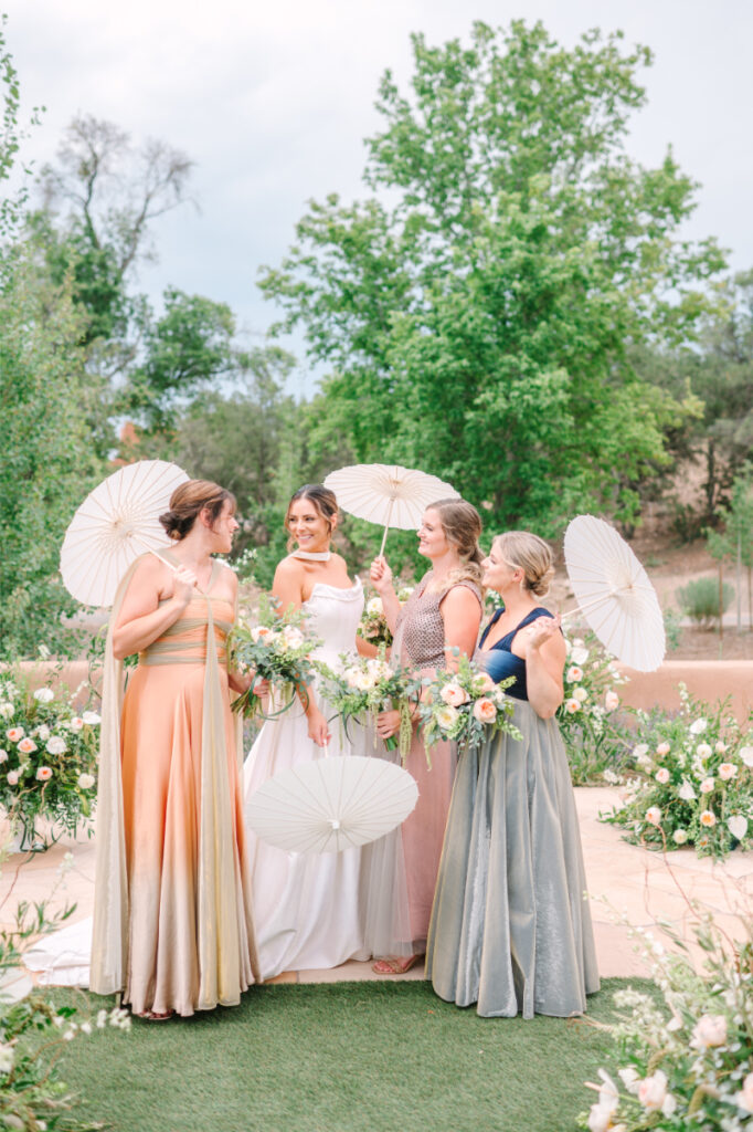 Bride stands surrounded by bridesmaids holding parasol umbrellas, as they admire the bride's luxury flower bouquet.