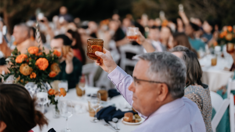 Guests lift drinks in the air after a toast is shared, one of the many wedding rehearsal dinner ideas for a more intimate and emotional evening.