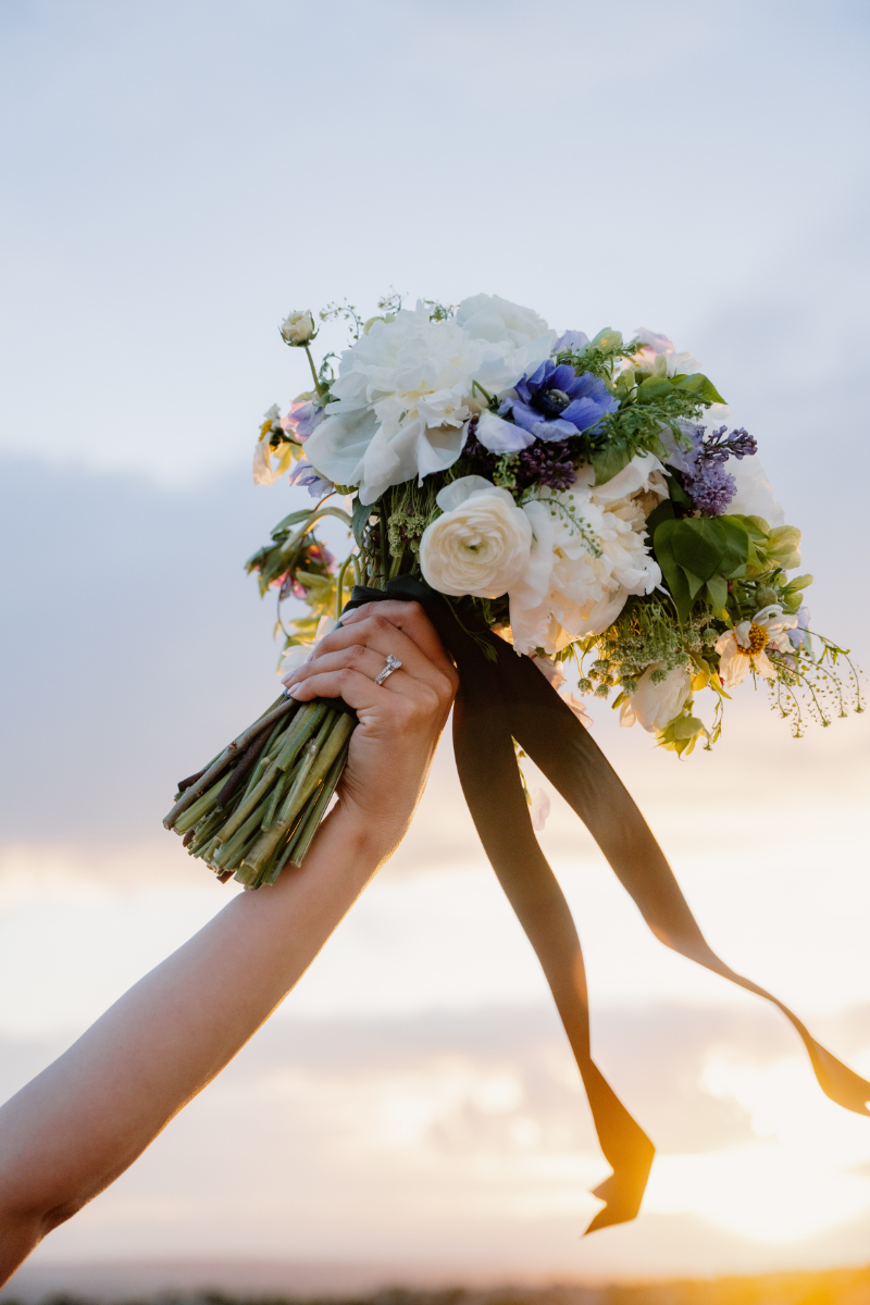 Bride holds up bouquet to be photographed in the sunset.