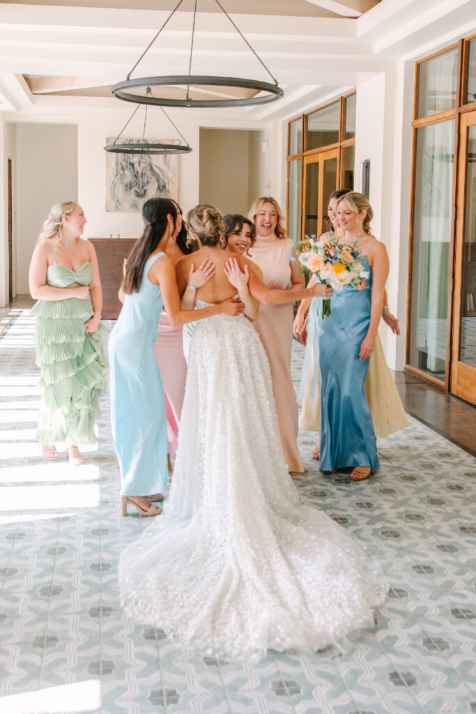 Bride hugging bridesmaids as she reveals her dress during a first look to them.