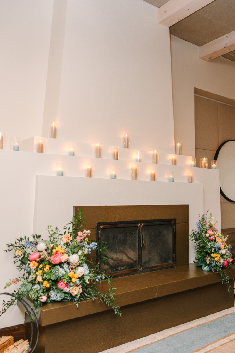 Fireplace surrounded by candles and large floral arrangements.