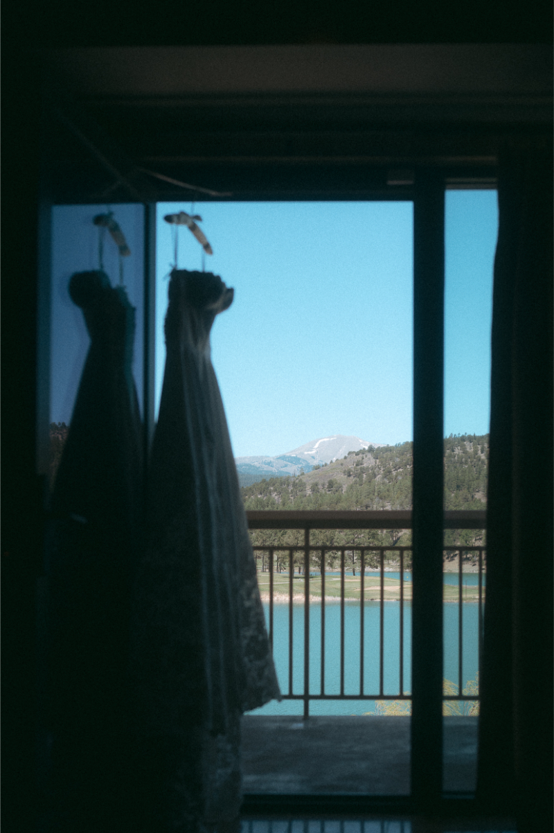 Wedding dress hanging on terrace, with mountain views and a lake below.
