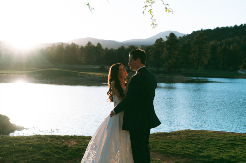 Bride and groom embrace during couples portraits in front of a lake during their Ruidoso wedding.
