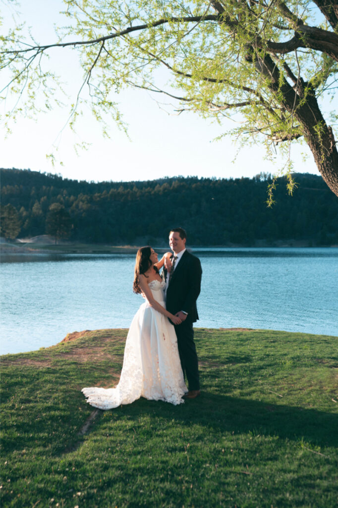 Bride and groom take portraits in front of lake backdrop during their Ruidoso wedding.