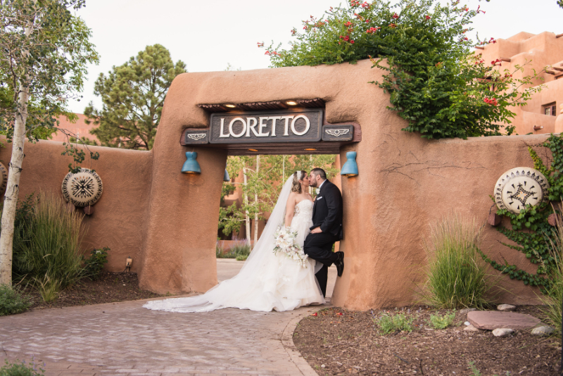 Bride and groom share kiss under adobe archway entrance to the Inn and Spa at Loretto.