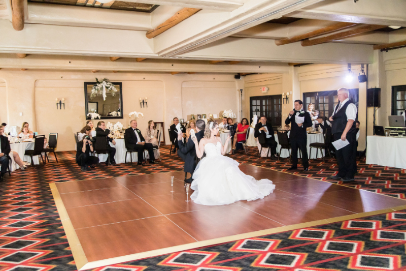 Bride and groom play the shoe game as they sit in chairs on the dance floor.