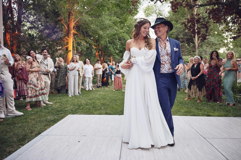 Bride and groom share their first dance on a dance floor placed in their backyard.