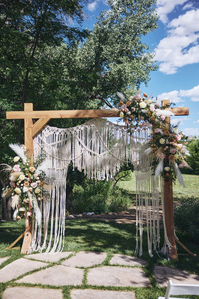 Wooden wedding ceremony arch with macrame draping and boho florals.