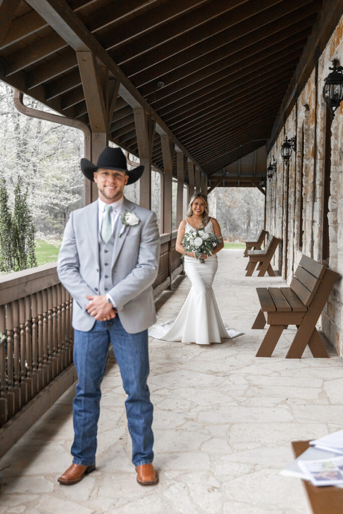 Bride and groom both stand facing the camera as the bride approaches the groom from behind to do their first look.