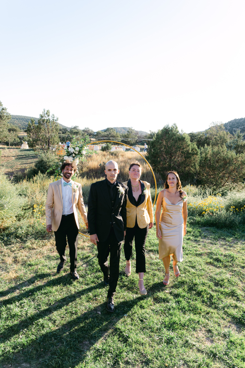Groom in all black suit struts with his wedding party members dressed in gold.