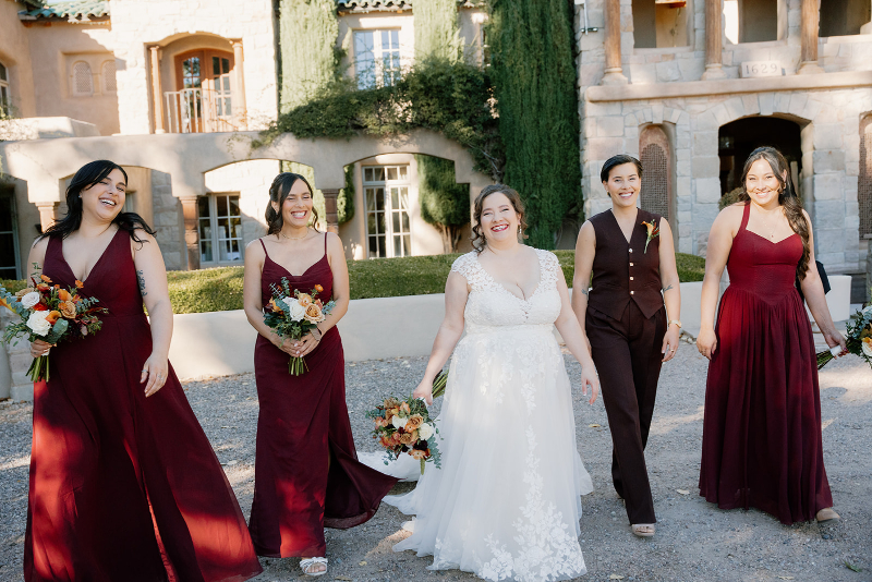 Bride walks with her bridesmaids on mansion lawn.