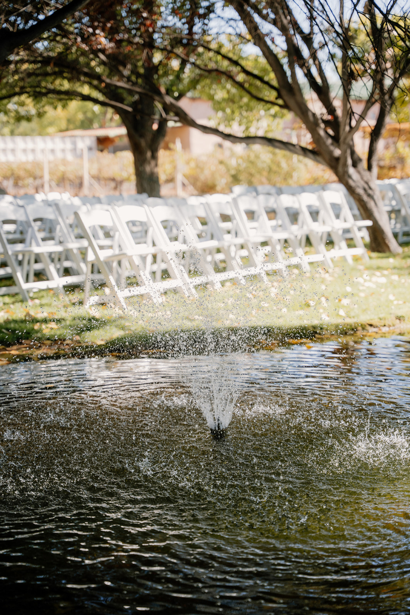 White folding chairs set up for ceremony on mansion lawn next to a fountain pond.