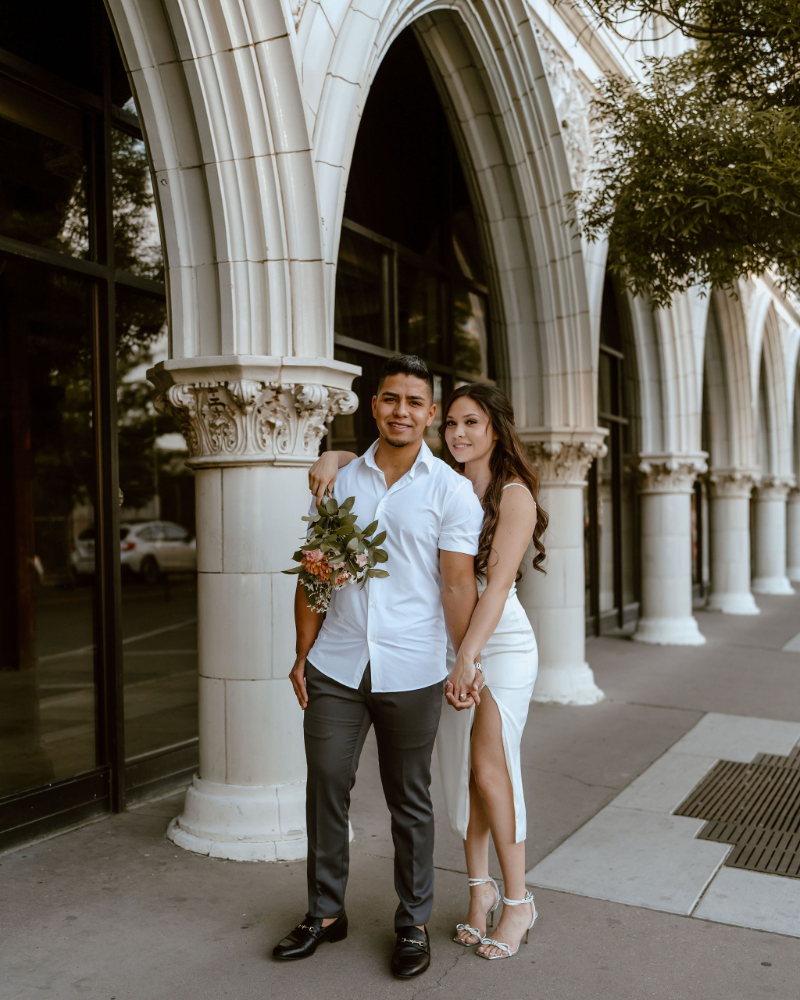 Engaged couple stand under building arch, enjoying a slow start to their wedding planning timeline.