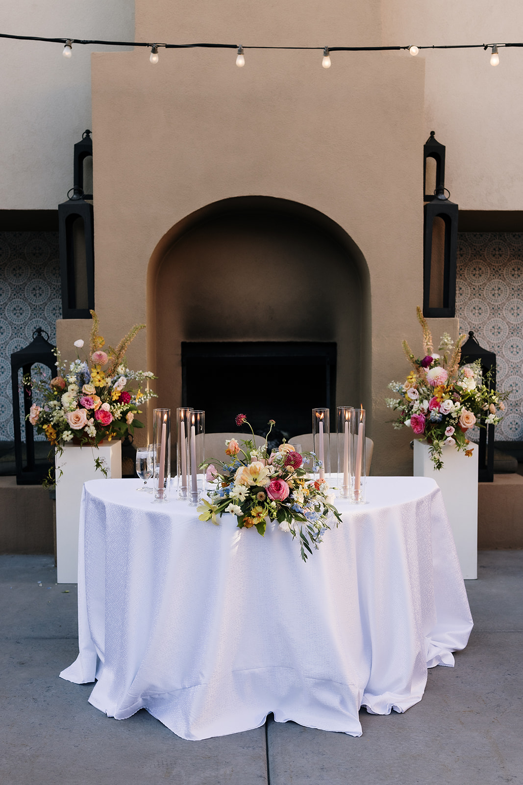 Sweetheart table decorated with white tablecloth, colorful floral arrangements, and taper candles in votives, perfect inspiration for a wedding vision board.