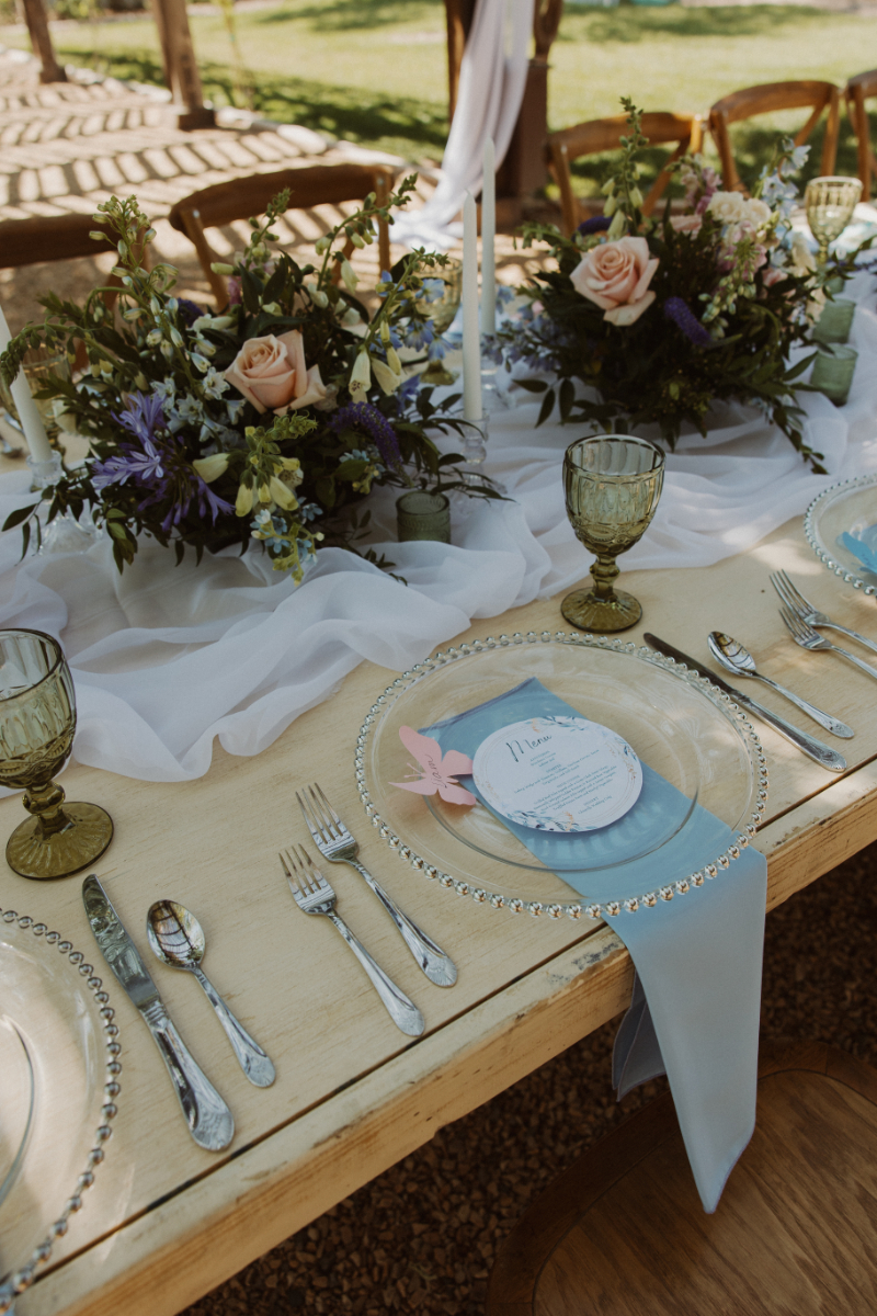 Table setting details with glass plate, pale blue napkin, butterfly name card, and floral centerpiece.