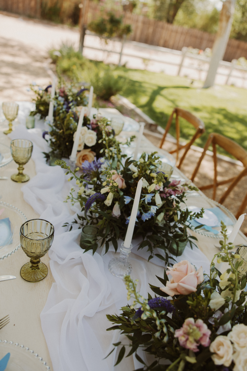 Floral centerpieces and taper candles sit lined along wooden table for French Chateau wedding.