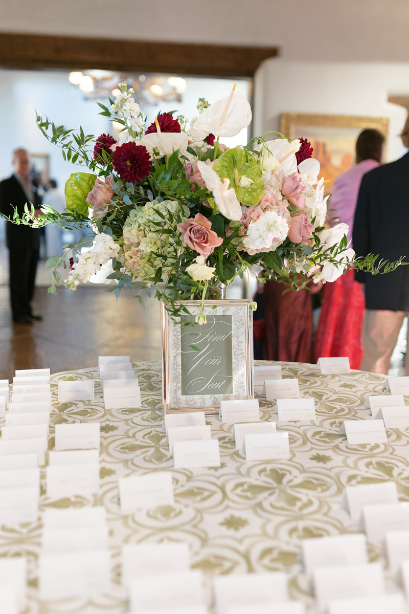 Escort cards sitting on table with patterned linen, beautiful floral arrangement sitting in the center.