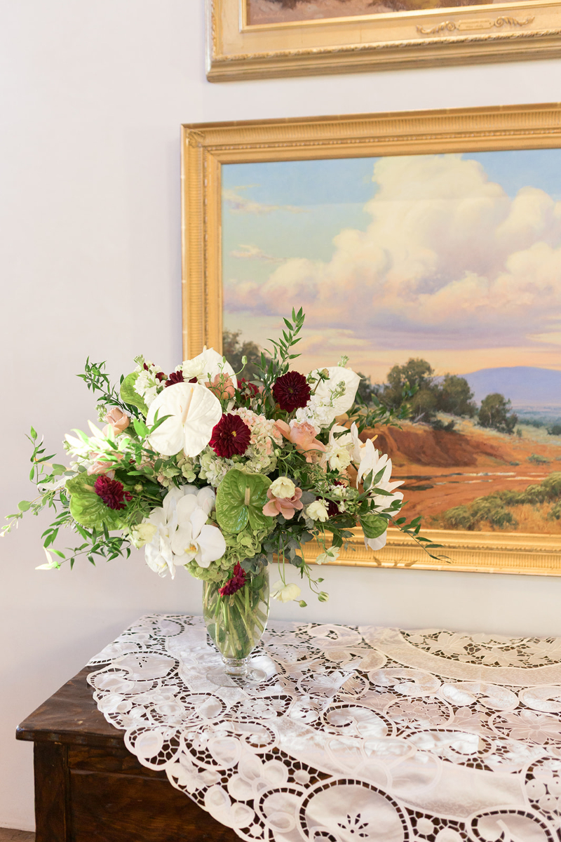 Floral arrangement sitting on top of lace applique on a wooden chest.