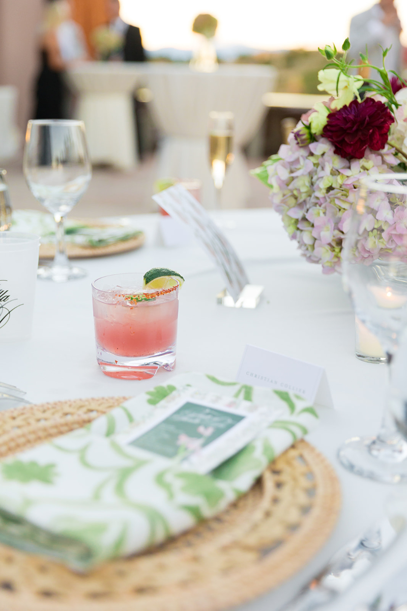Pink prickly pear margarita sitting next to guests table setting.