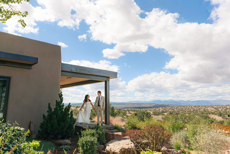 Bride and groom stand on porch of Santa Fe weddings venue that overlooks the beautiful surrounding landscape.