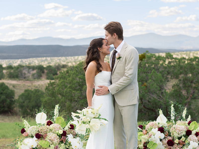 Groom kisses bride on the forehead as they stand for a photo during their Santa Fe weddings portraits that overlook the landscape below.