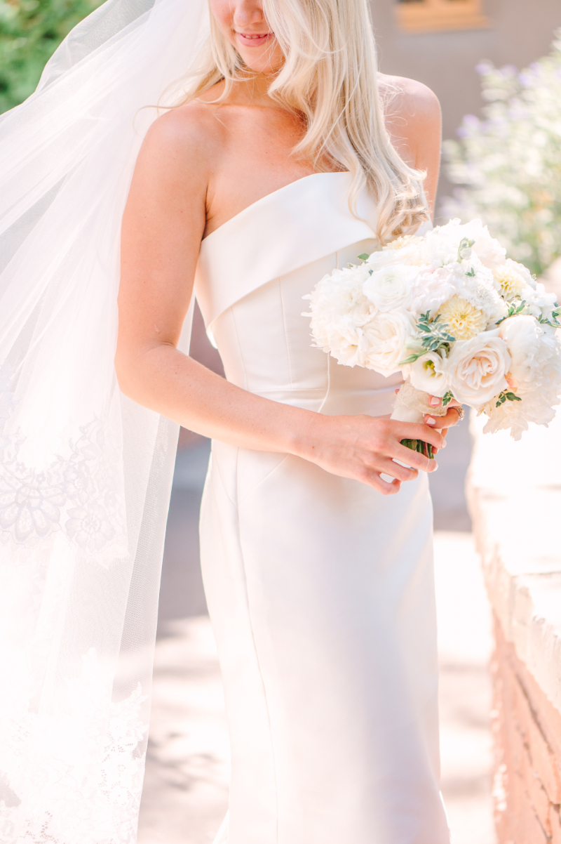 Bride stands holding her bouquet as she looks down at the ground, a great example of bridal bouquet ideas in Santa Fe.
