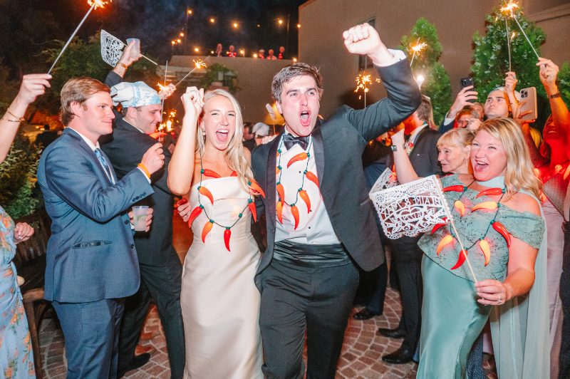 Bride and groom exit reception with fists in the air as their guests cheer them on.