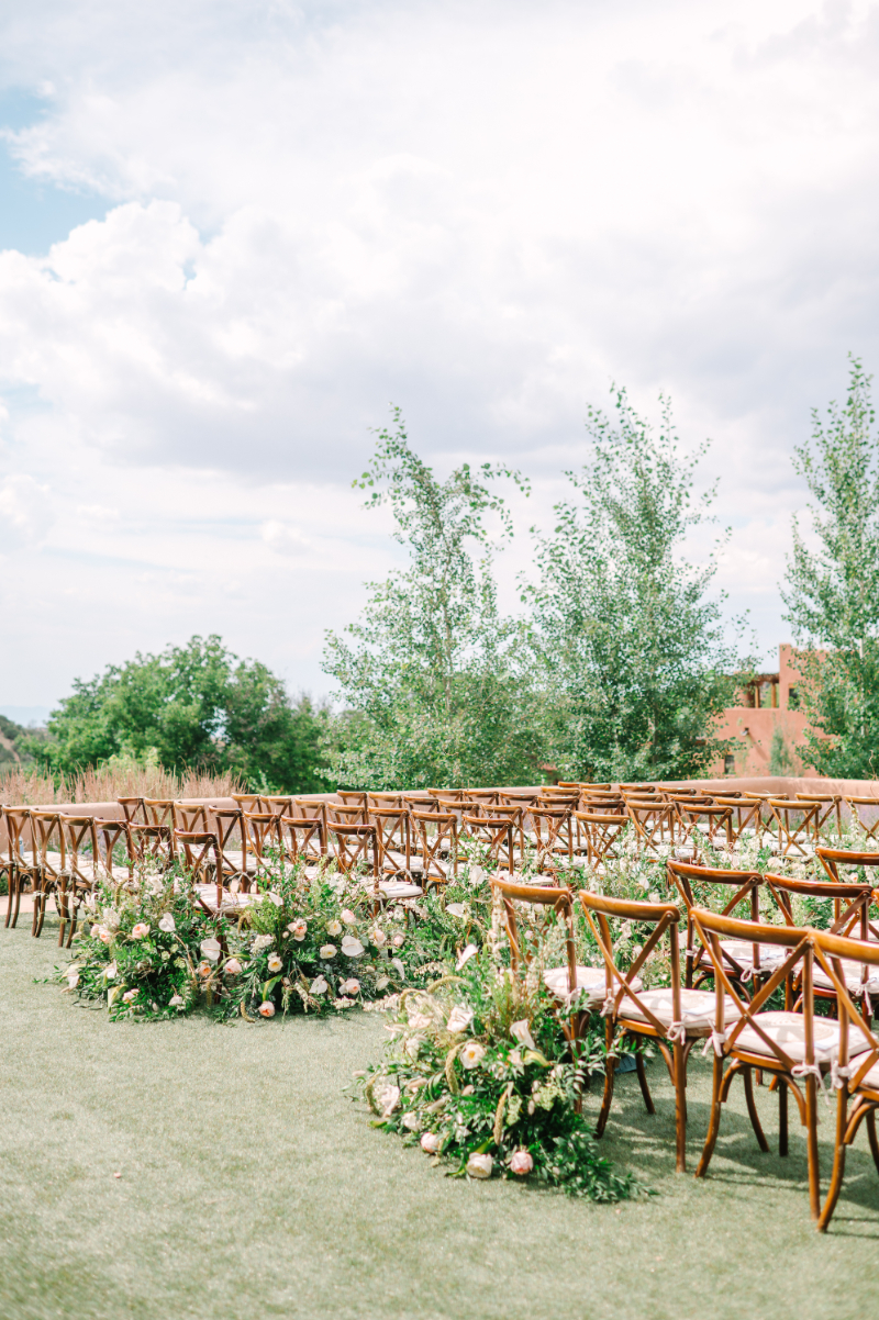 Ceremony set up with wooden chairs and end of aisle adorned with ground floral arrangements.
