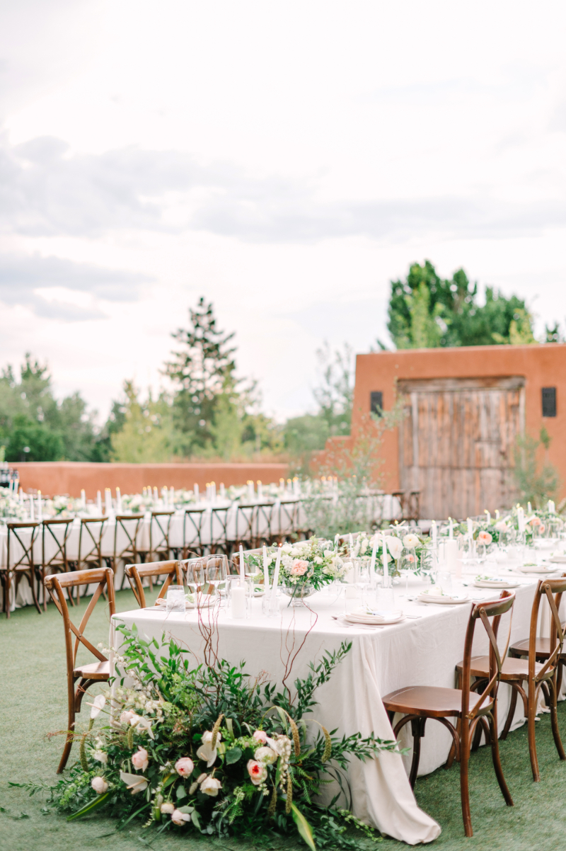 Reception tables set with white tablecloths, ground floral arrangements, and floral centerpieces.