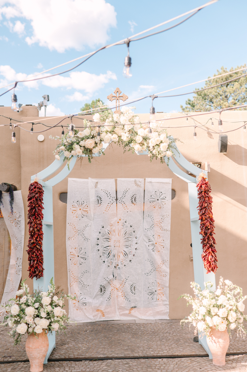 Ceremony arch covered in white florals and red chilis.
